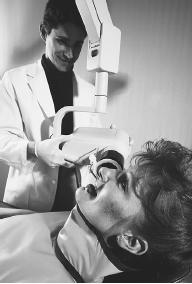 "SOFT" X-RAY MACHINES, SUCH AS THIS ONE BEING USED BY A DENTIST TO PHOTOGRAPH THE PATIENT'S TEETH, OPERATE AT RELATIVELY LOW FREQUENCIES AND THUS DON'T HARM THE PATIENT. (Photograph by Richard T. Nowitz/Corbis. Reproduced by permission.)