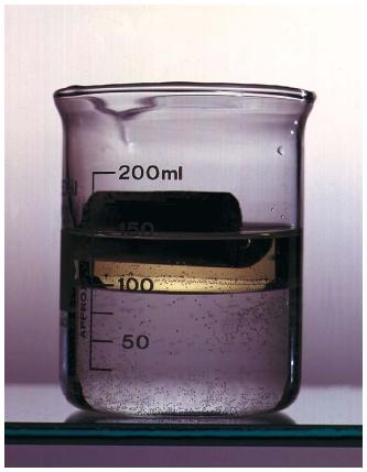 The oil in this beaker is layered on top of the water because it is less dense than the water. Similarly, the cork floats on the oil because it is less dense than either the oil or the water. (Reproduced by permission of Phototake.)