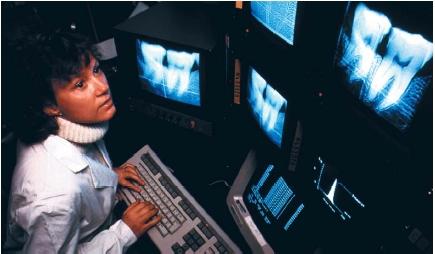 A dentist examining a patient's teeth using digital subtraction radiography, a computerized X-ray technique. This new technology reveals details of the teeth and surrounding gum and bone tissue that traditional X rays cannot detect. (Reproduced by permission of Photo Researchers, Inc.)