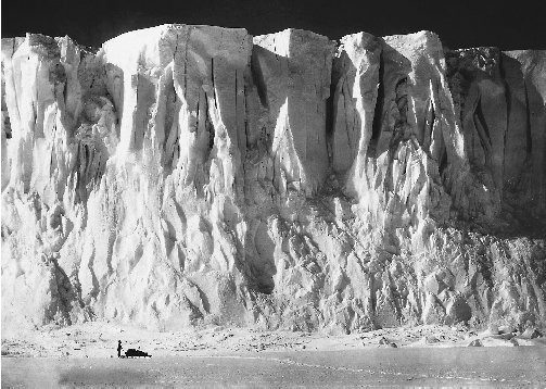 This mammoth Antarctic glacier dwarfs the scientist at its base. Glacial ice cores give scientists a historical record of climate changes.