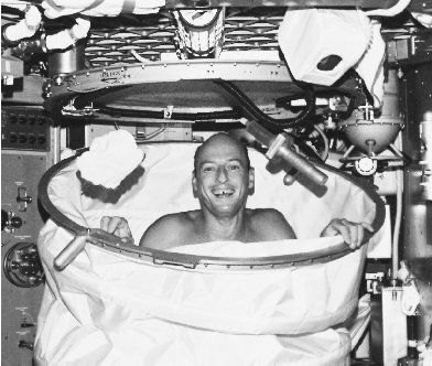 A Skylab astronaut smiles after a hot shower in the collapsible, sealed stall. Only three gallons of water per shower were allowed on the station.